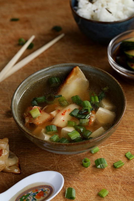 Miso soup is garnished with potstickers, tofu, green onions, and kimchi for a delicious and healthy appetizer or meal. 