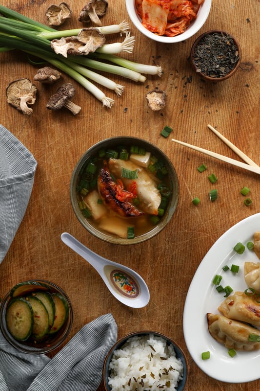 A restaurant-ready bowl of miso soup is served with side dishes like kimchi, potstickers, and cucumber salad. Filled with tofu and other treats, miso soup is an excellent meal starter.