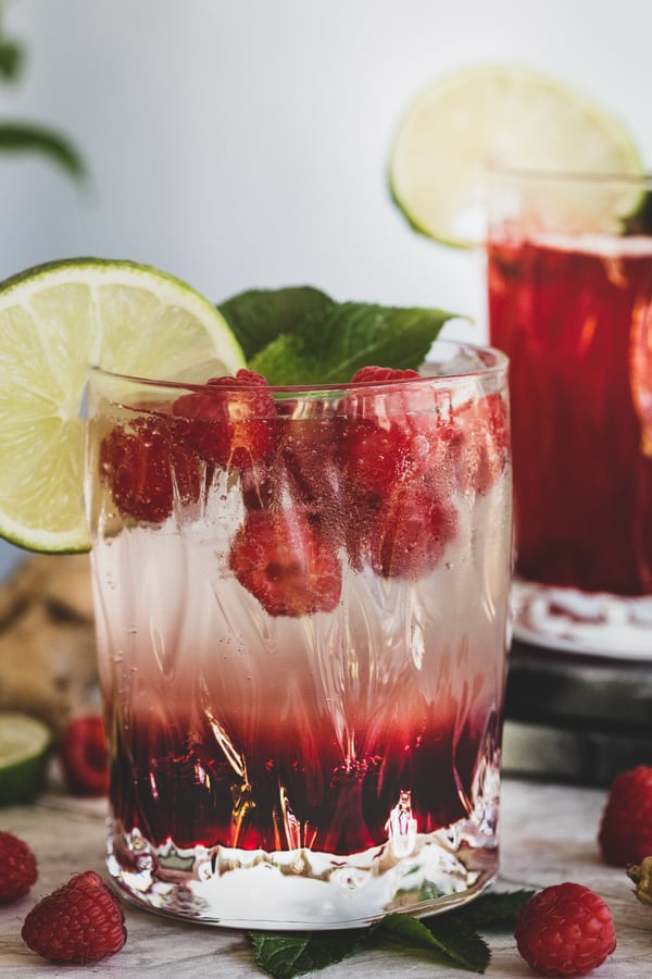 Ginger Berry mocktail sparkling in the summer sun, surrounded by raspberries.