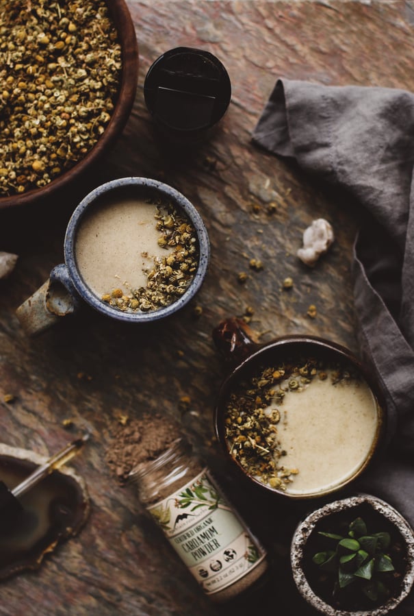 Mugs of hot drinks and cardamom powder spilling out of bottle. 