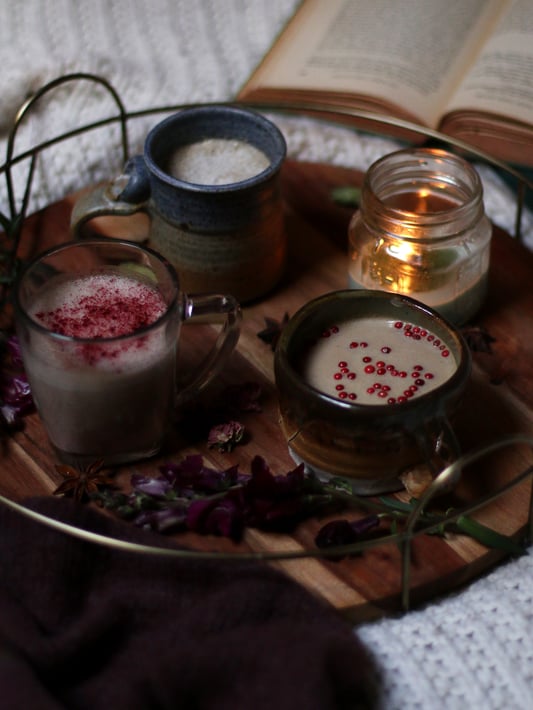 Three variation of moon tea for nighttime relaxation arranged on a tray with a candle. Warm milk and alternative milk drinks garnished with herb powders and pink peppercorns. 