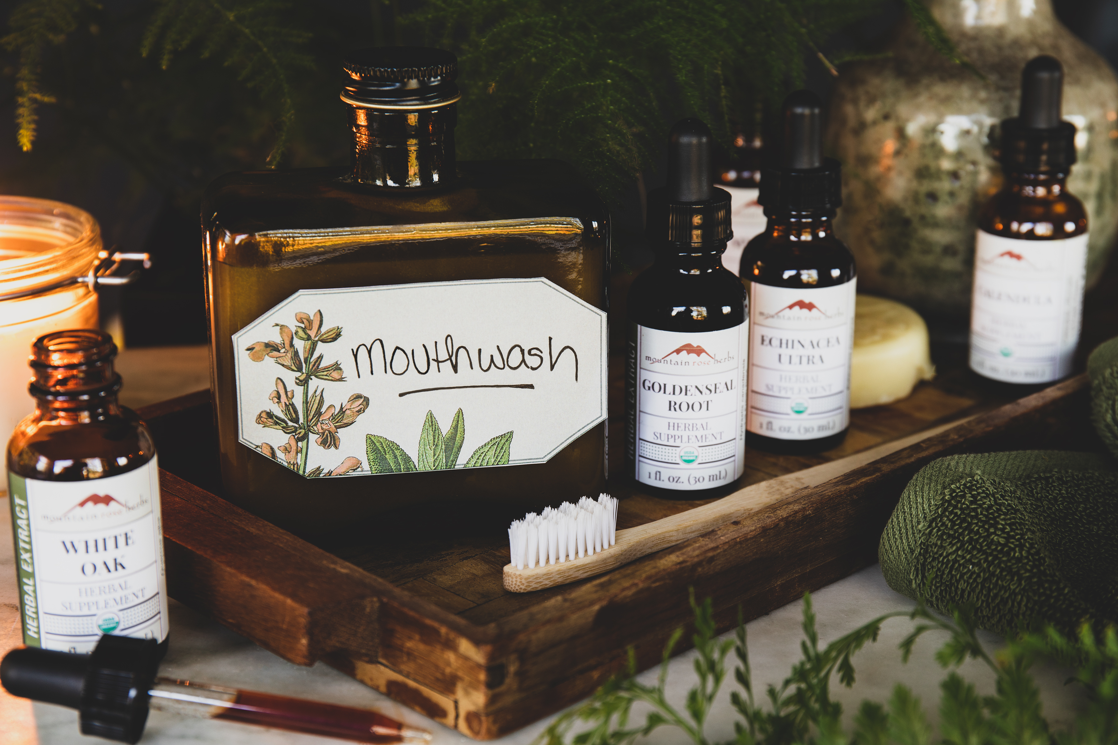 Bottle of homemade mouthwash with bottles of tinctures and a wooden toothbrush. 