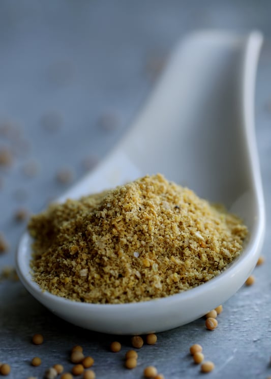 White spoon with mustard powder in it and whole mustard seeds artistically  spilled on table