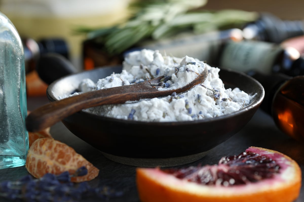 Bowl of natural herbal carpet deodorizer powder with wooden spoon surrounded by citrus slices.