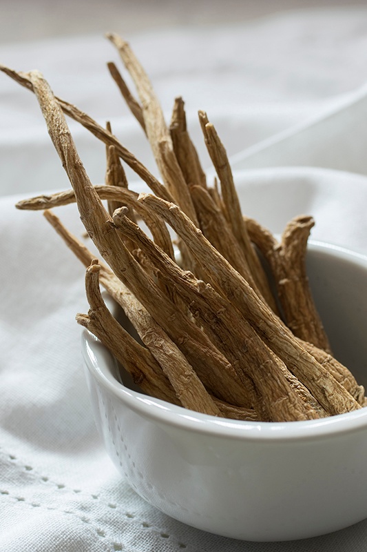 Ginseng roots in a white porcelain bowl on a white linen tablecloth