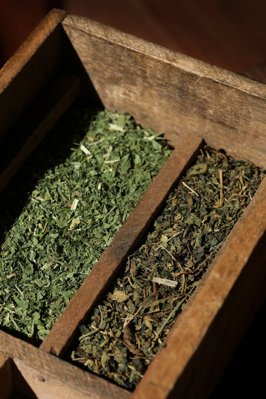 Dried organic North American nettle leaf and European nettle leaf side by side in antique wooden tray.