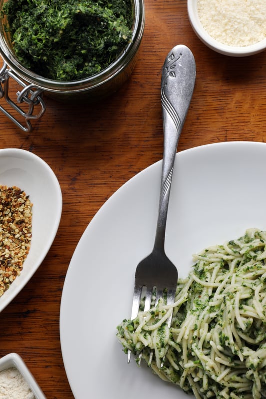 Fork on white plat sitting next to nettle pest pasta near nettle pest ingredients