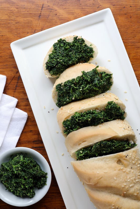 Platter with loaf of French bread sliced showing nettle pesto spread in between slices