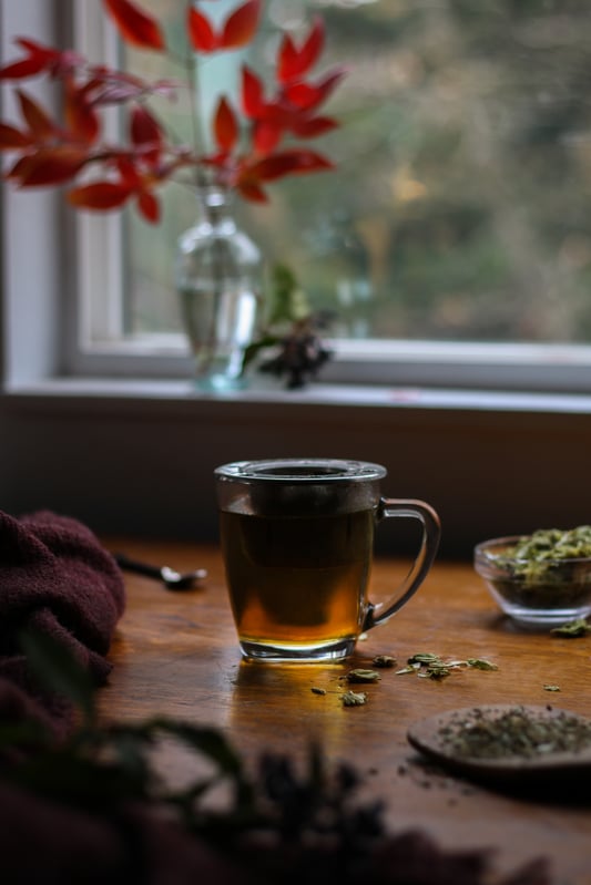 Nighttime herbal tea blend featuring hops flowers, mugwort, and catnip. Brewing in a clear glass mug, an amber tea steeps in a tea strainer before bedtime.