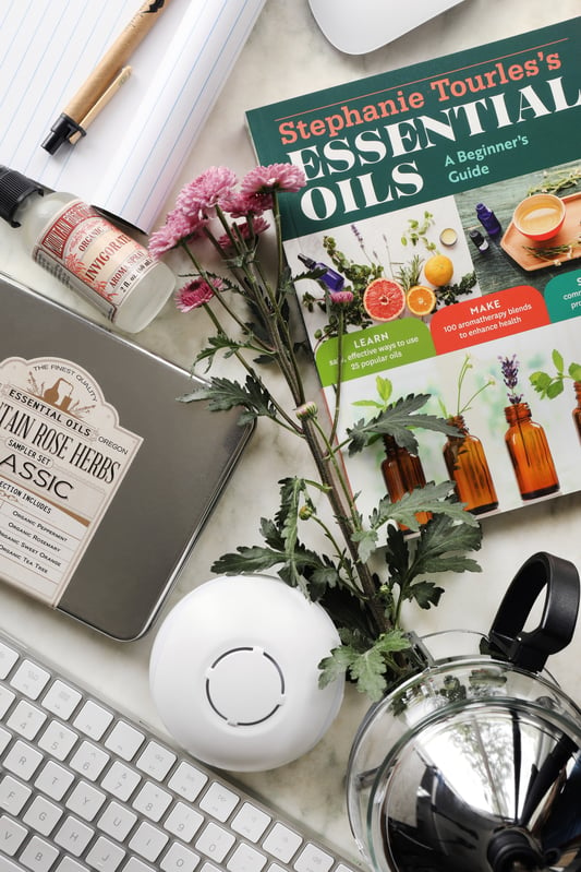 Gifts for an office mother arranged among office supplies such as a note pad, and keyboard. Essential oils, a tea pot, and aroma sprays.