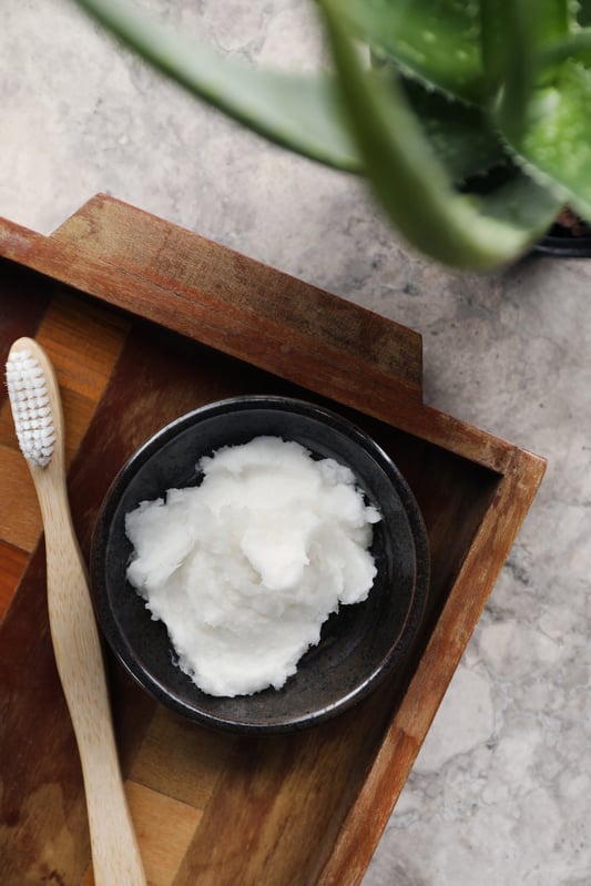 Photo of white whipped homemade toothpaste next to a crisp clean wooden toothbrush. 