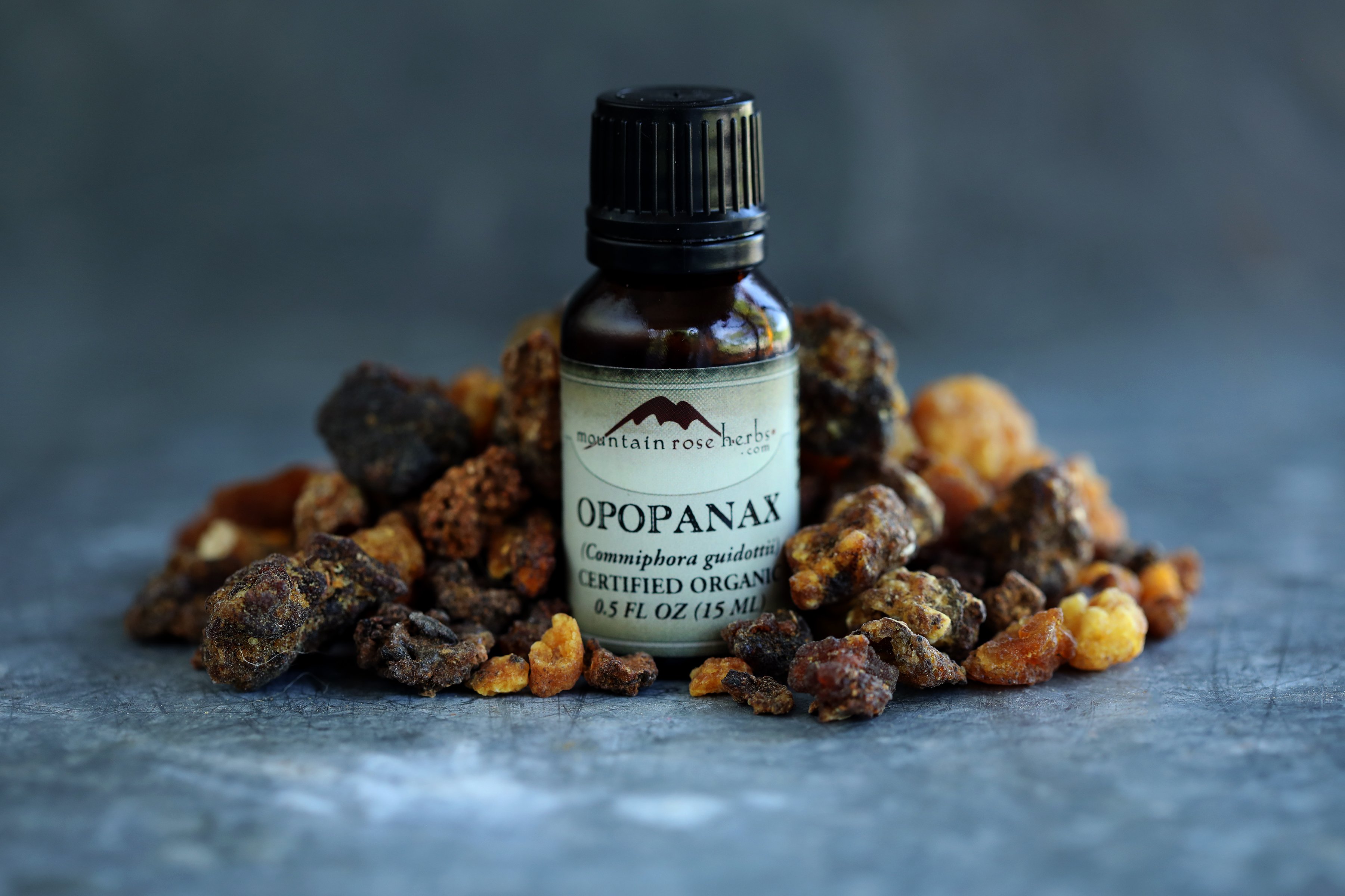 Opopanax resin and essential oil arranged together on a slate counter top. Dark orange and brown resin pieces. 