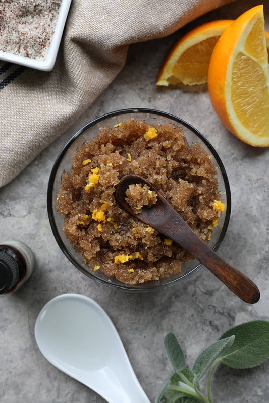 Clear bowl with warm brown body scrub with bright orange flecks. 