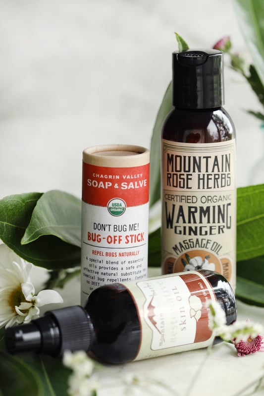 Gifts for an outdoorsy woman. Bug repellent, skin oil, and massage oils, all arranged among spring green foliage. 