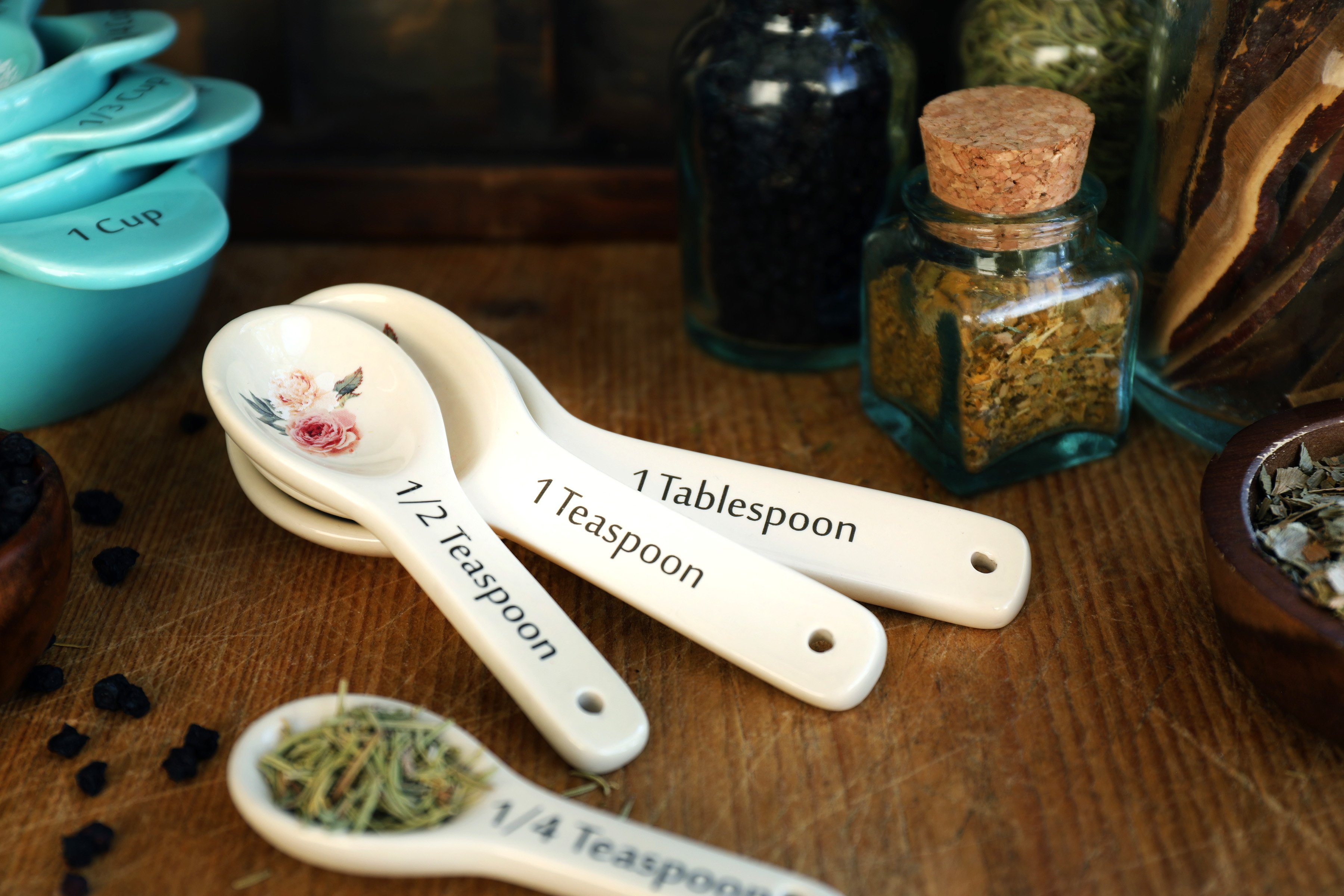 Fancy vintage measuring spoons are adorned with painted flowers and used to add organic rosemary leaf into herbal formulas by parts. 