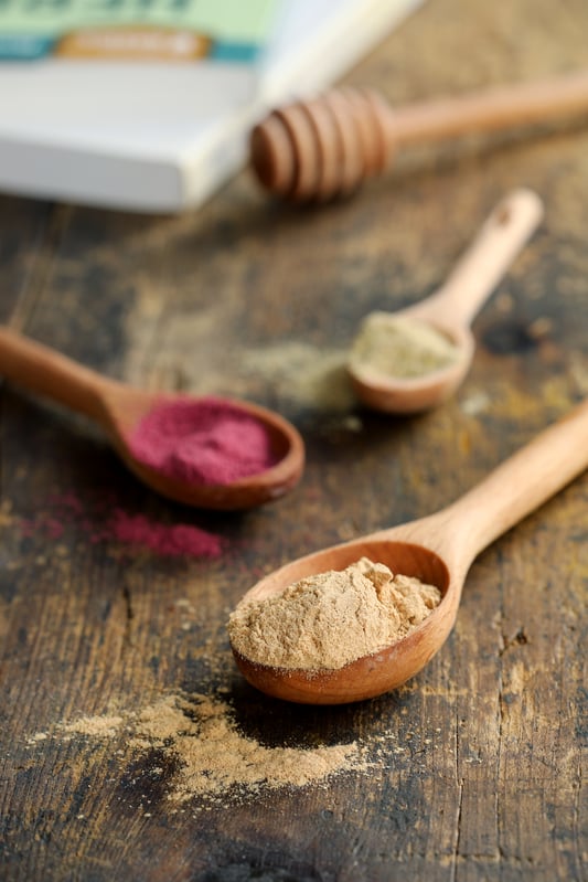 Wooden spoons with colorful powdered herbs spilling out on a rustic wooden table.