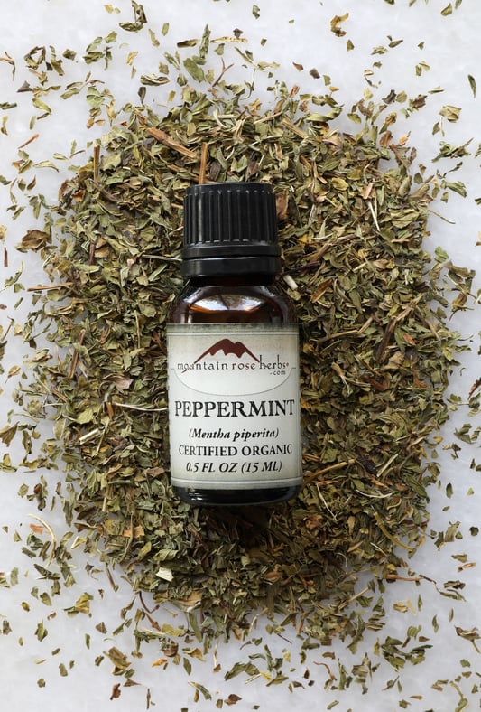 Half Ounce Bottle of Organic Peppermint Essential Oil laying on top of dried peppermint leaves