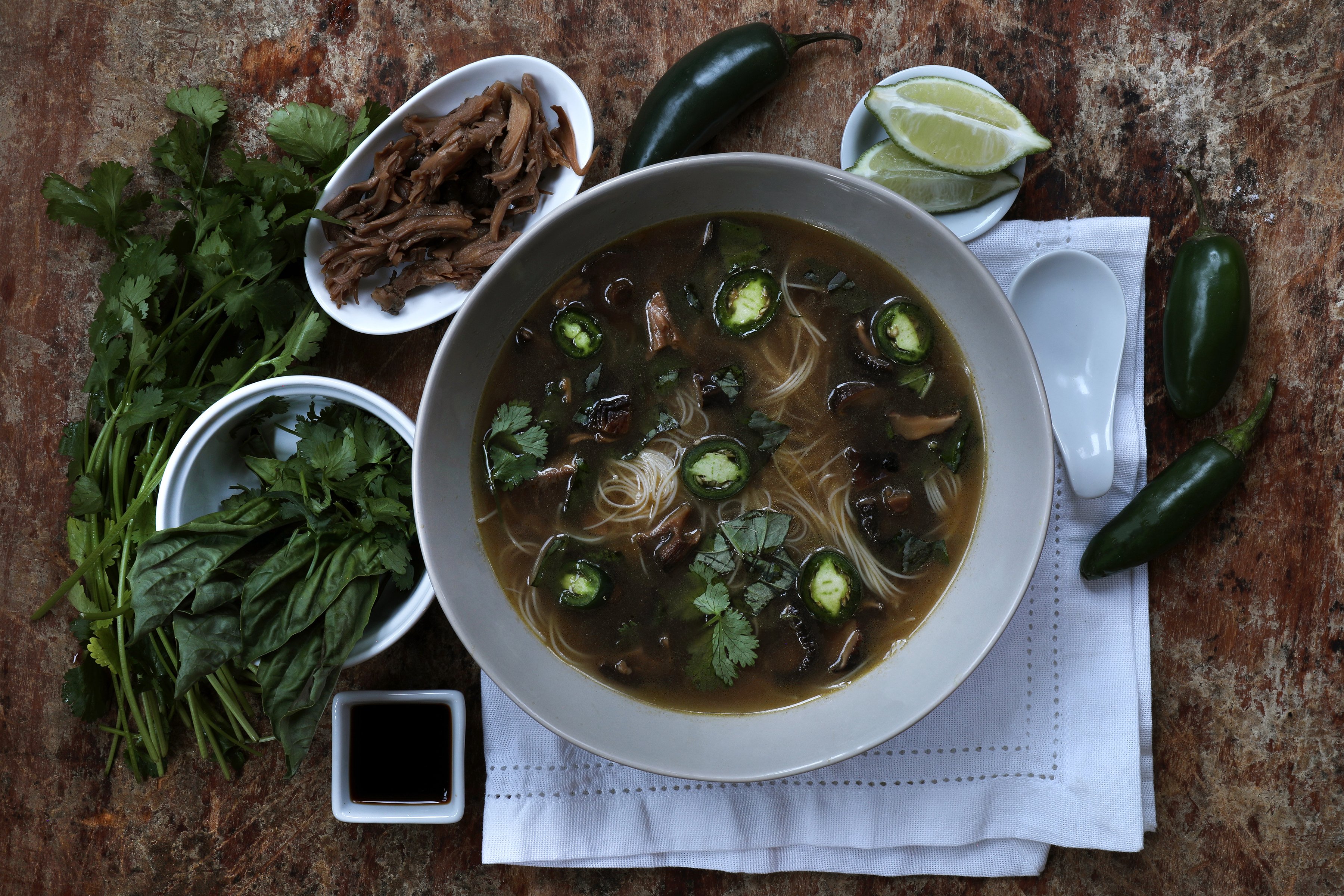 Bowl of pho soup with fresh ingredients around it. 