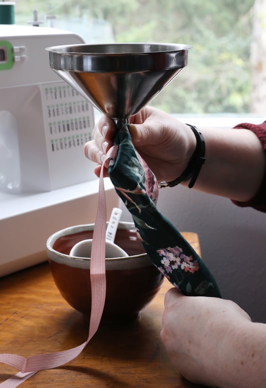 Hands using funnel to pour lavender and buckwheat into homemade eye pillow