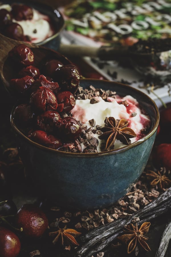 Bowl of yogurt with poached cherries and botanical garnishments