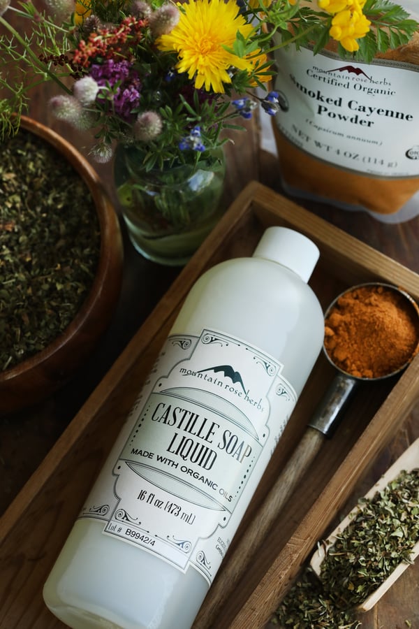 A bottle of castille soap with cayenne powder to make natural pest control garden spray. Colorful bee-friendly flowers in the background. 