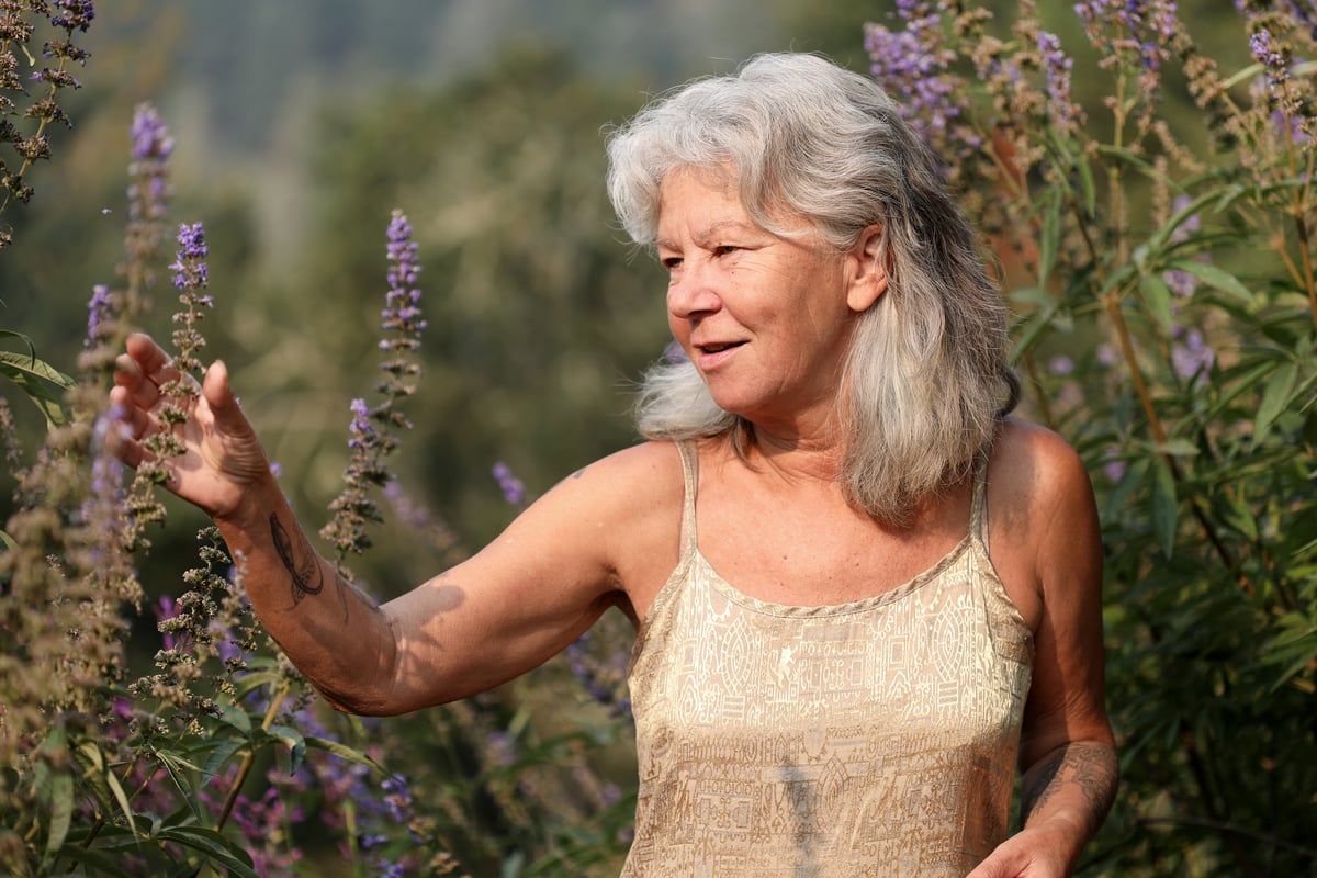 Beautiful gray-haired woman admiring the purple blossoms that are attracting pollinators in her garden