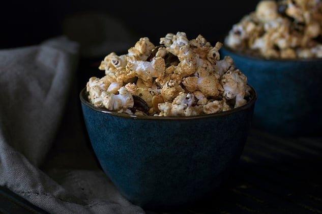 Blue bowl stuffed with caramel popcorn in front of a dark grey background