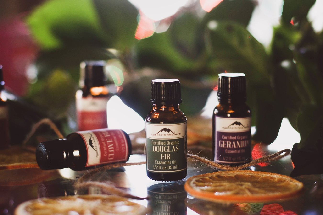 Essential oils on a table with greens ready to blend to make diy potpourri.