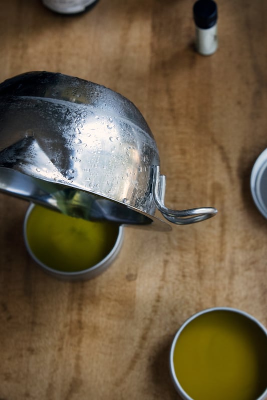 Pouring warm salve ingredients into tins on wooden table