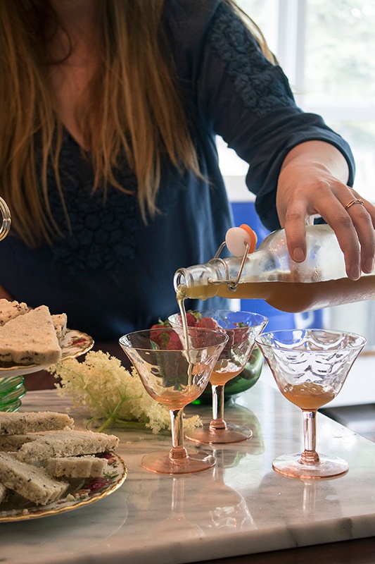 Woman pouring simple syrup into cocktail glasses next to fresh bread and flowers, entertaining