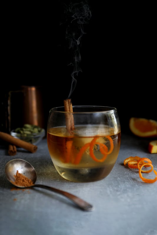 Pumpkin pie spice Old Fashioned in a lowball garnished with a smoking cinnamon stick and orange rind.
