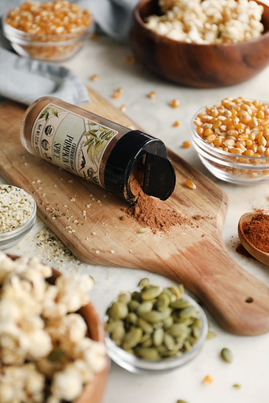Ingredients for making sweet and spicy popcorn at home. Pumpkin pie spice, popping corn, chipotle powder, pumpkin seeds, and hemp seeds come together for a perfect fall snack.