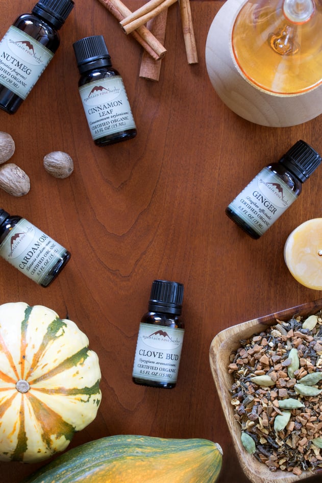 Ginger, Cardamom, and Clove Bud Essential Oils on table with candles, herbs, and pumpkins