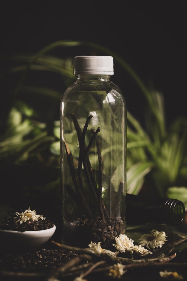 clear glass bottle with sticks inside with plants in the background