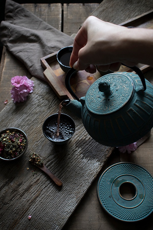 Pouring tea into small teacup on wooden table 