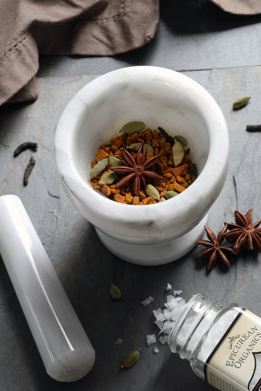 Whole cardamom and star anise and dried turmeric in mortar with pestle on counter