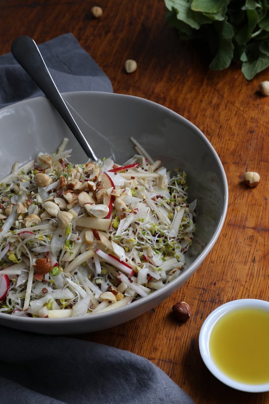 Sprout Salad in a bowl with chopped hazelnuts and radish, with a  serving spoon and fork