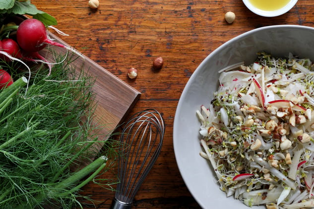 plate of sprout salad on counter top with whisk and radishes and celery