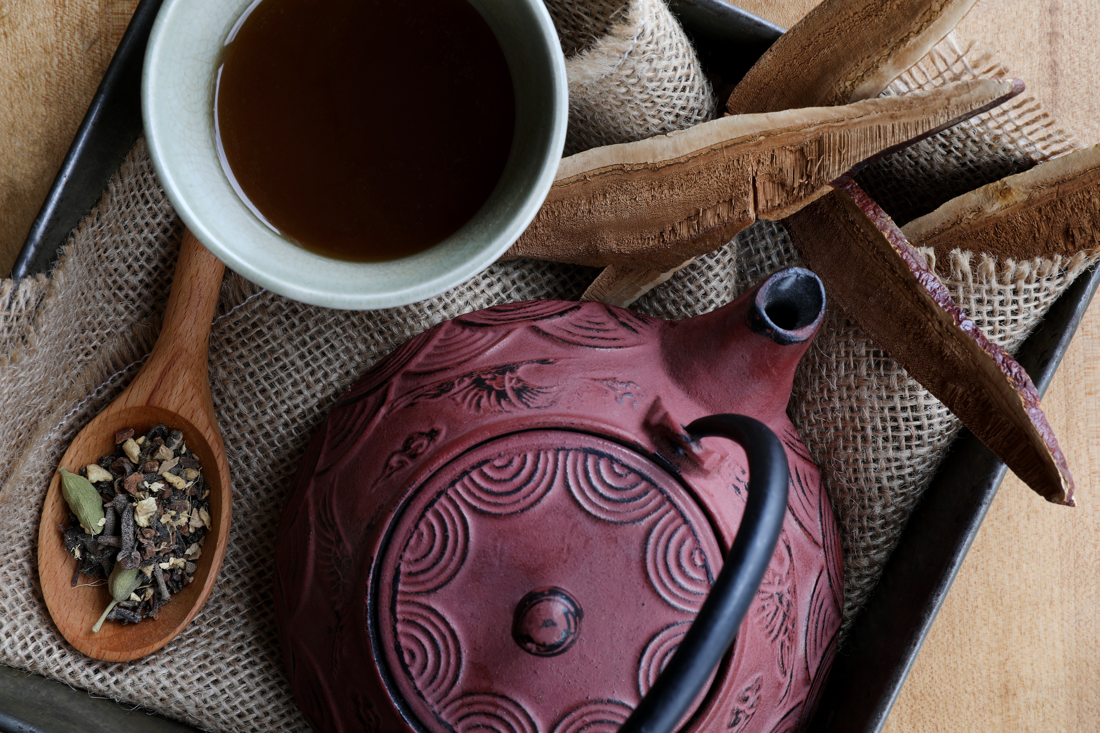 Red cast iron teapot with cup of hot tea, spoon of chai ingredients and Reishi mushroom slices