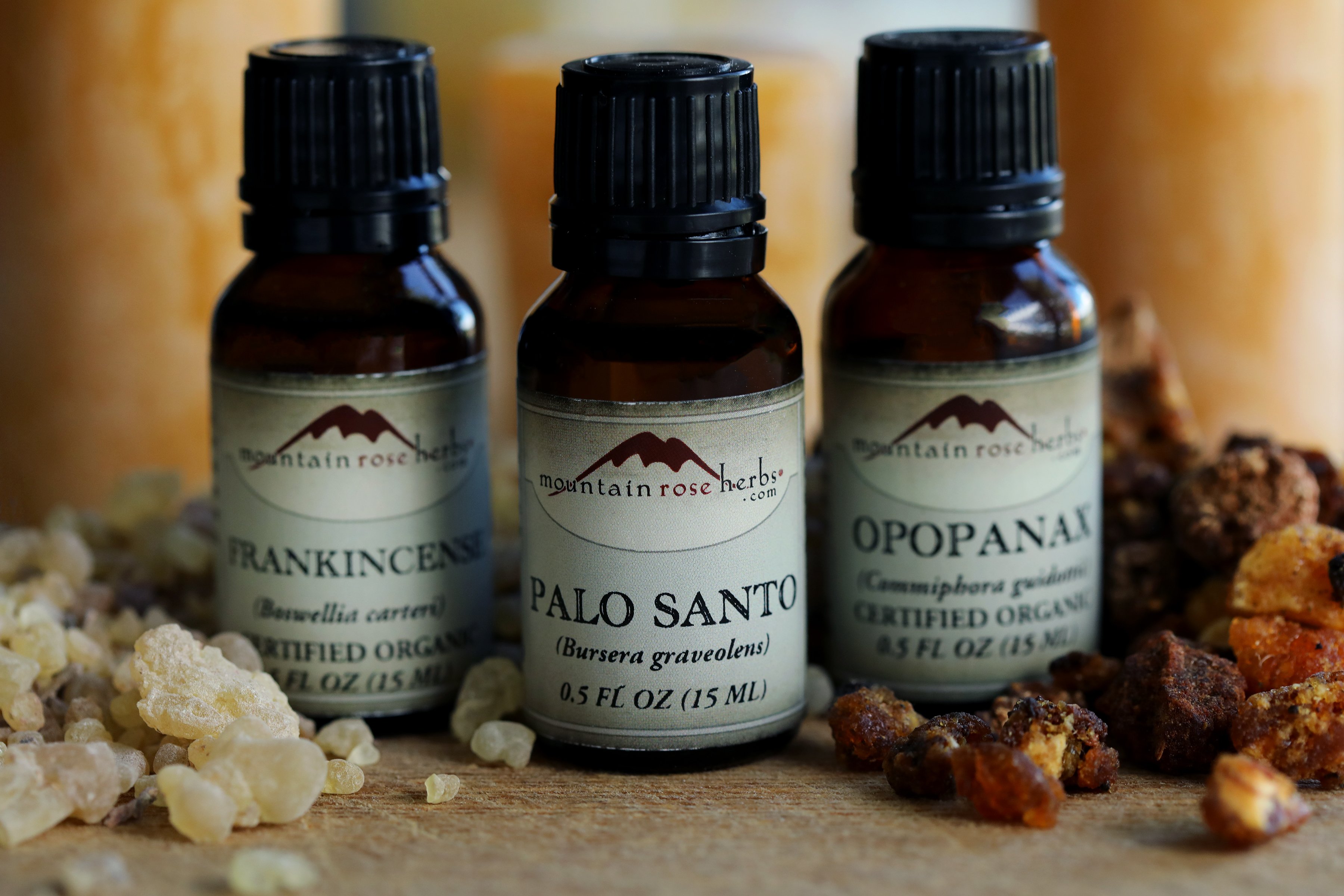 Three bottles of essential oil resting between frankincense and opopanax resins in their hard form. Beeswax candles are in the background. 