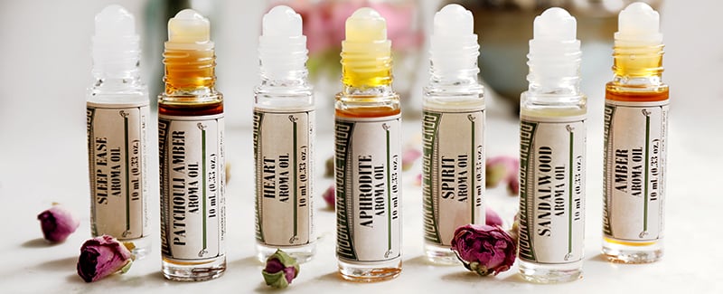 Line up of roll-on aroma oils offered by Mountain Rose Herbs. Seven different essential oil blends intended for perfume use assorted together with dried rose buds. 