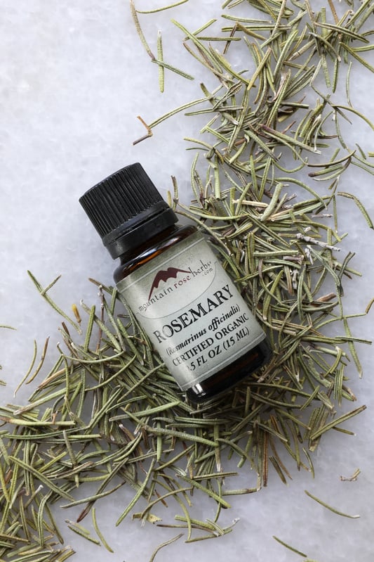 1/2 oz. bottle of rosemary essential oil laying on rosemary leaves