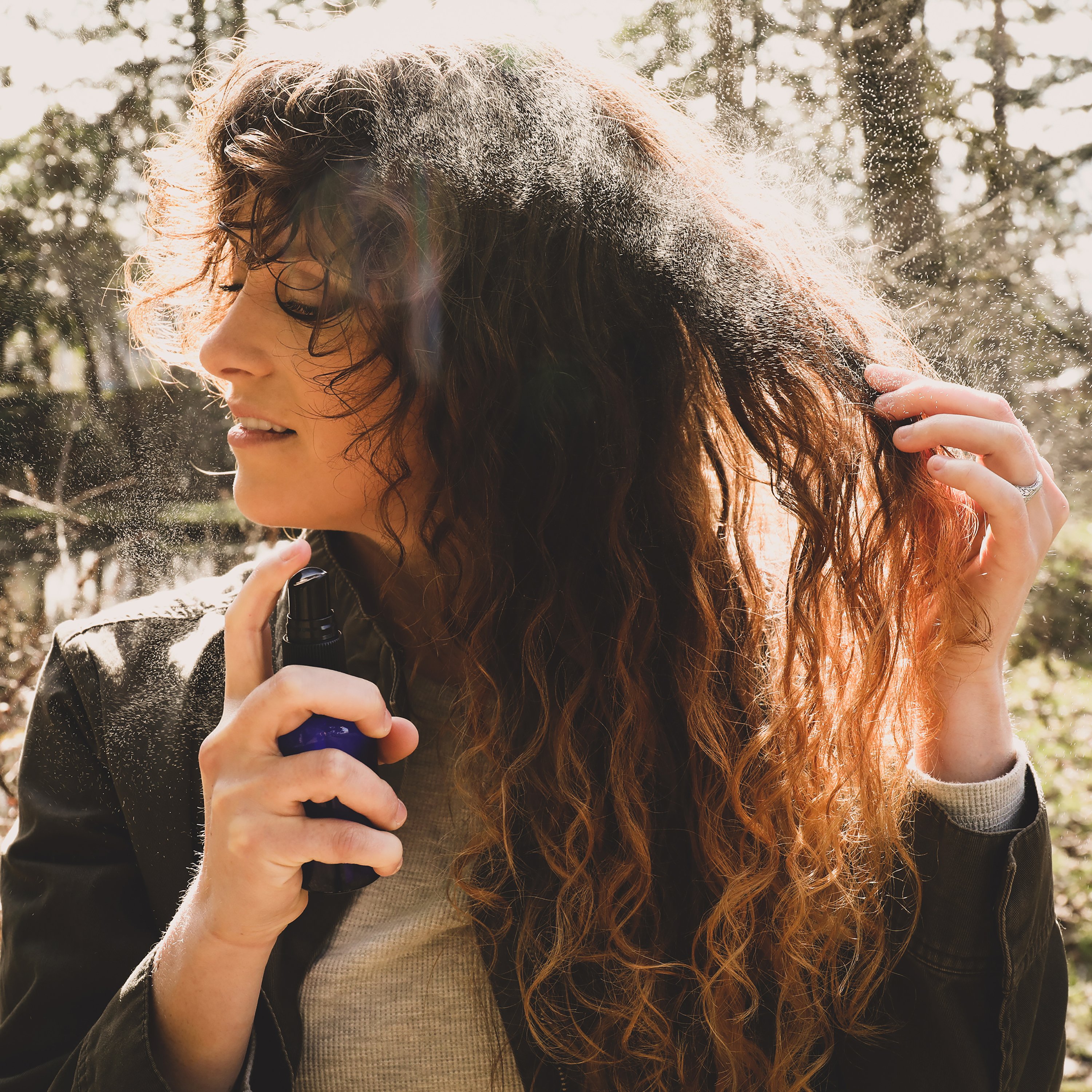 Young woman spraying beautiful curly hair. 