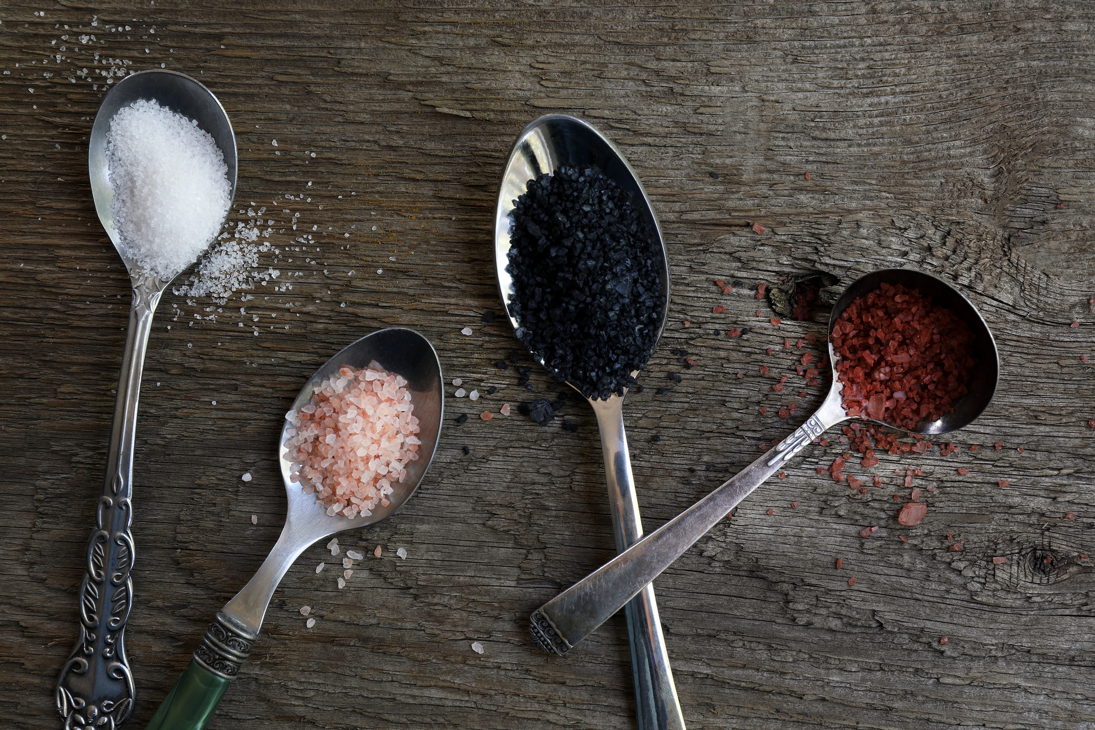 Spoons of colorful salts on wooden board