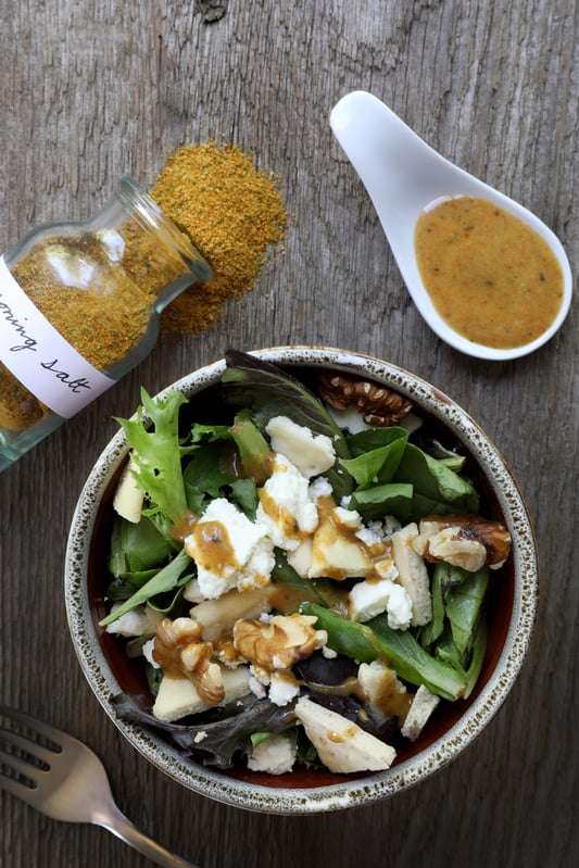 Bowl of salad with bottle of seasoning salt and salad dressing on spoon