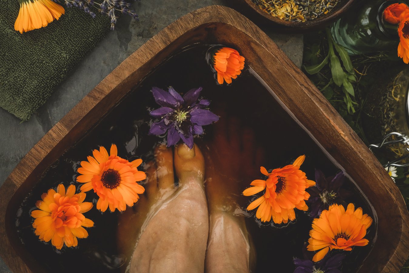 Feet soaking in herbal soak with orange and purple flowers