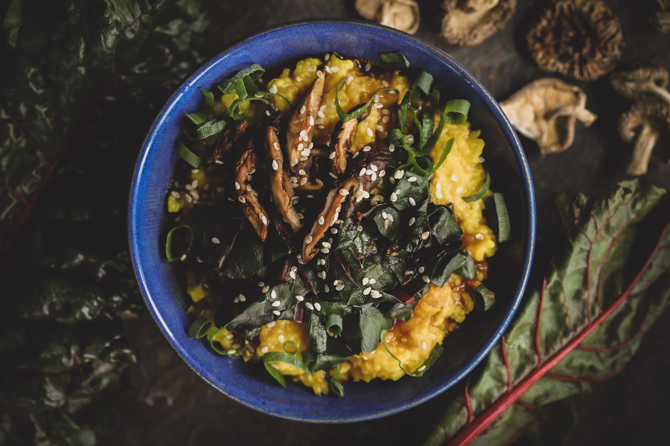 Golden congee in a vibrant blue bowl with sliced mushrooms and greens- garnished with sesame seeds. 