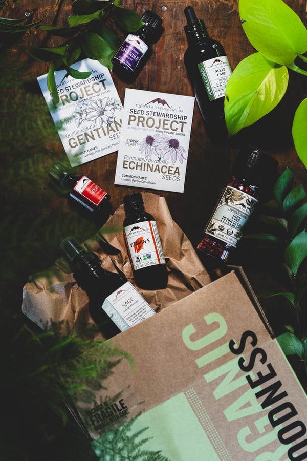 A Mountain Rose Herbs shipping box spills on the table with various herbal products and packets of Echinacea and Gentian seeds from the Seed Stewardship Project.