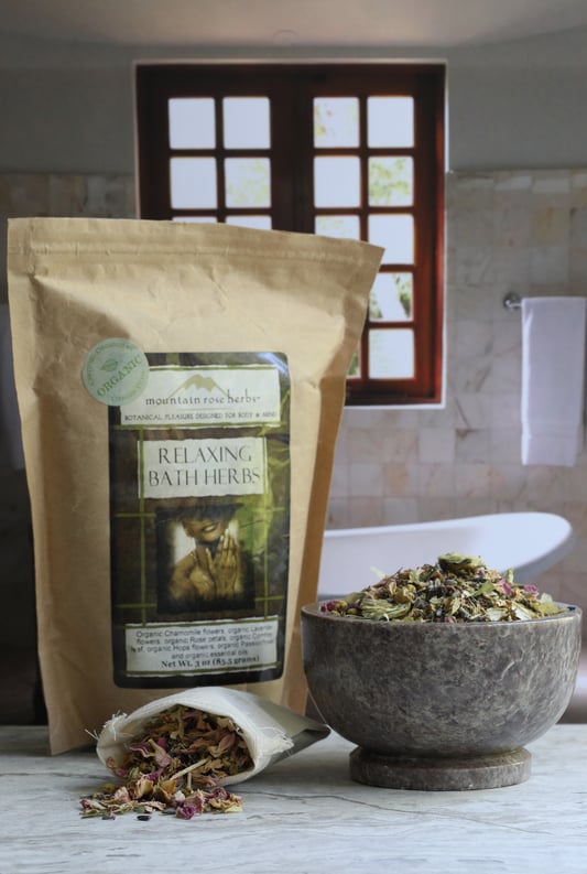 Paper bag and mortar and muslin bag filled with relaxing bath herbs sitting on counter outside of tub