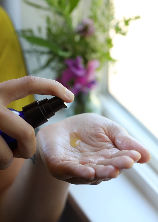 Skin serum is being dispensed from a cobalt bottle. A dollop of green tea serum in a woman's palm. 